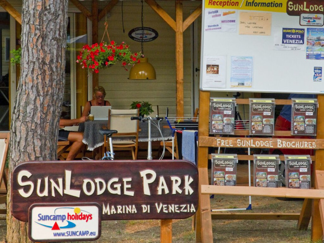 Espace accueil et information au SunLodge Park, Marina di Venezia, Italie, avec brochures et visiteurs.