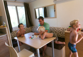 Una familia juega a un juego de mesa en una cabaña moderna, sentados alrededor de una mesa de madera.