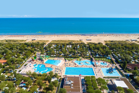 Aerial view of a resort with swimming pools, slides, greenery and direct access to a sandy beach.