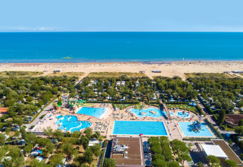 Aerial view of a resort with swimming pools, slides, greenery and direct access to a sandy beach.