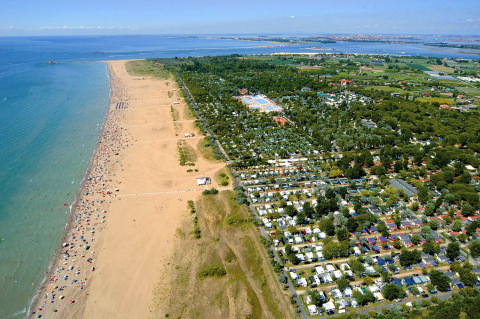 Luchtfoto van een vakantiepark aan een breed zandstrand, met stacaravans en veel groene natuur erbij.