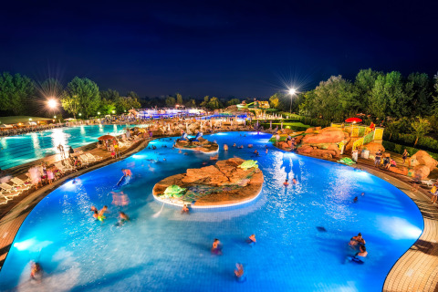 Piscina iluminada en un lodge de noche, con huéspedes disfrutando del agua y el ambiente relajado.