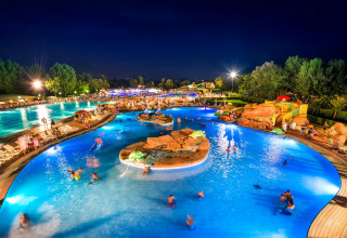 Piscina iluminada en un lodge de noche, con huéspedes disfrutando del agua y el ambiente relajado.