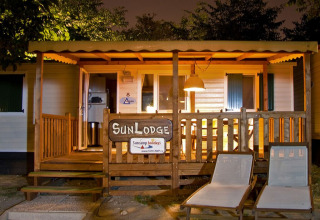Aftenbillede af SunLodge Redwood hytte med oplyst veranda, træhegn og to loungestole udenfor