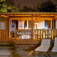 Aftenbillede af SunLodge Redwood hytte med oplyst veranda, træhegn og to loungestole udenfor
