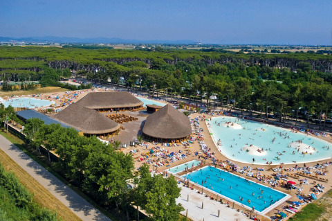 Vista aérea de un gran lodge con techos de paja, piscinas y muchos huéspedes rodeados de árboles verdes.