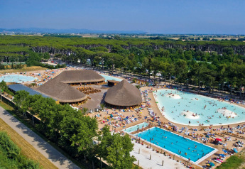 Vista aérea de un gran lodge con techos de paja, piscinas y muchos huéspedes rodeados de árboles verdes.