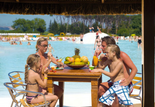 Familie nyder drinks og dessert ved et bord ved poolen på en lodge, omgivet af andre gæster.