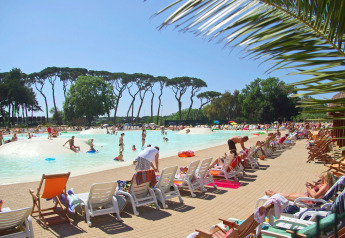 Piscina exterior en un lodge con personas tomando el sol y nadando, rodeada de árboles y tumbonas.