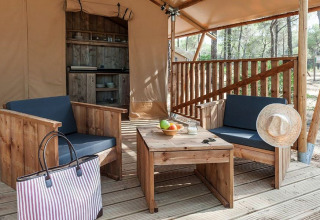 Alojamiento glamping con muebles de madera, cocina pequeña, frutero y sombrero de paja en el bosque.