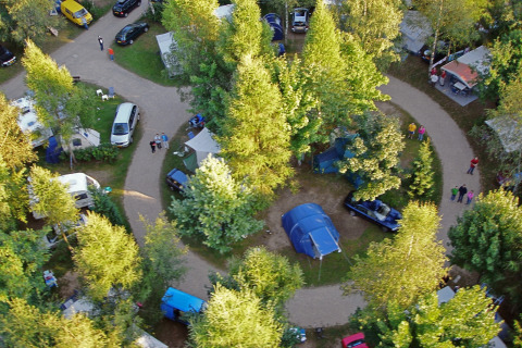 Vista aérea de un camping con coches, tiendas y una tienda safari rodeado de frondosos árboles verdes.