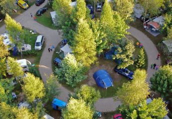 Aerial view of a campsite with cars, tents, and a safari tent surrounded by lush green trees.