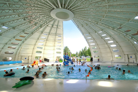 Piscina coperta dentro una grande tenda safari, con bambini e adulti, luce diurna penetrante.