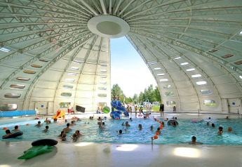 Piscina cubierta dentro de una gran carpa de safari con niños y adultos, luz natural entrando.