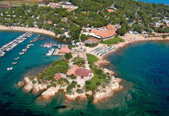 Vista aerea di un lodge pittoresco sul mare, con porticcioli, alberi e spiagge attrezzate.