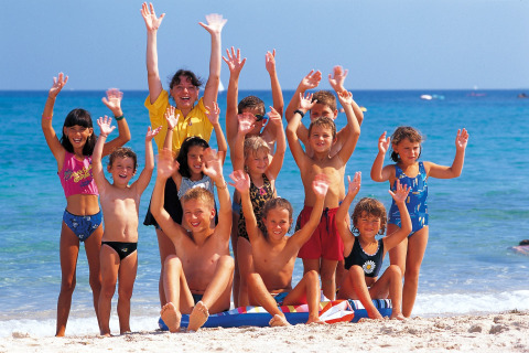 Un groupe joyeux d’enfants et un adulte saluent sur la plage en vacances près d’un lodge au bord de la mer.
