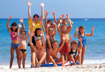 Un grupo alegre de niños y un adulto saludan en la playa junto al mar durante unas vacaciones en el lodge.