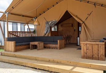 Terraza cubierta con sofás y muebles de madera en SunLodge Taiga, Camping Cisano/San Vito, Italia.