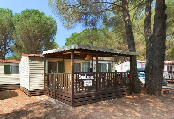 Foto af SunLodge Redwood-hytte i en skov, med overdækket terrasse og træer omkring, solrig dag