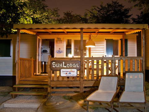 Vue de nuit du SunLodge Redwood, terrasse en bois éclairée, chaises longues et ambiance chaleureuse.