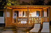 Vista nocturna de SunLodge Redwood con porche de madera, iluminación cálida y sillas tumbonas.