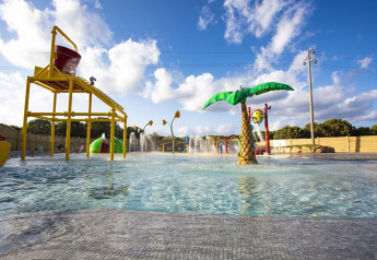 Buitenspeelparadijs met water bij een lodge met kleurrijke speeltuigen, palmbomen en fonteinen onder de zon.