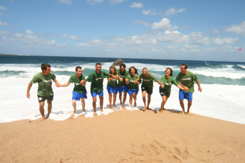 Een groep mensen in groene T-shirts houden elkaars hand vast terwijl ze samen het strand oplopen.
