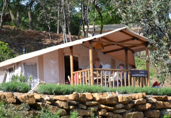 Twee mensen zitten op de veranda van een SunLodge Safari-tent, omgeven door bomen en natuurstenen.
