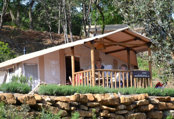 Twee personen ontspannen op de veranda van een SunLodge Safari-tent in een bosrijke omgeving.