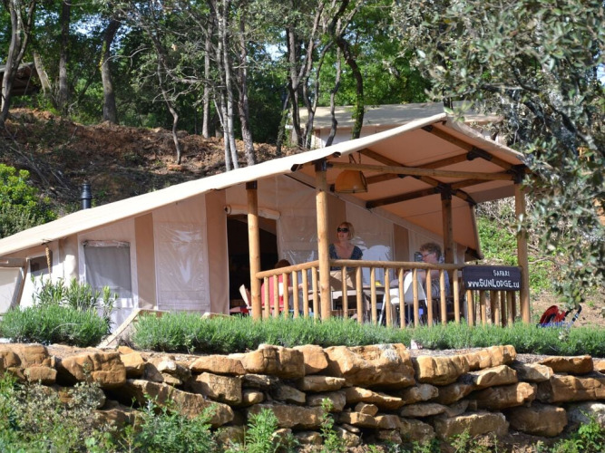 Dos personas disfrutan en la terraza de una tienda SunLodge Safari rodeada de árboles y naturaleza.