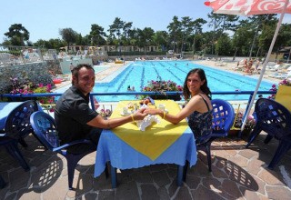 Una pareja sonriente sentada en una mesa cerca de una piscina en un albergue, rodeados de flores y sillas.