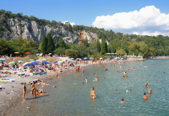 Persone si godono una giornata di sole su una spiaggia di ciottoli davanti a scogliere e ombrelloni.