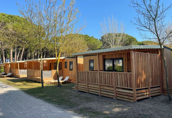 Cabañas de madera en SunLodge Sabai, Camping Union Lido Mare en Italia, rodeadas de árboles y naturaleza.
