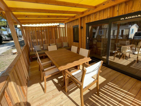 Udendørs spiseområde med træmøbler på en træterrasse under en gul markise ved SunLodge Sabai i Italien.