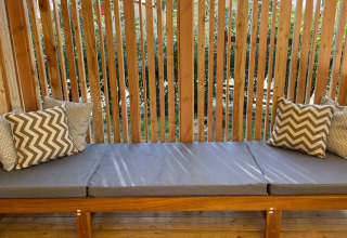 Banco exterior con cojines grises y almohadas decorativas en SunLodge Sabai, Camping Union Lido Mare, Italia.