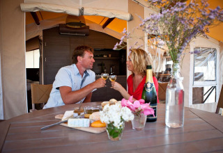 Pareja disfrutando vino y comida en Sunlodge Safari en Camping Union Lido Mare, Italia, con flores en la mesa.