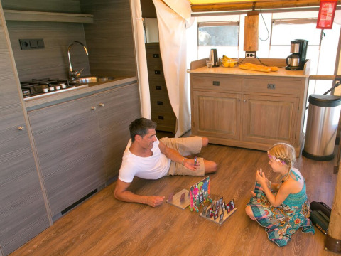 Hombre y niña juegan a un juego de mesa en el suelo de una cocina Sunlodge Safari en Camping Union Lido Mare, Italia.