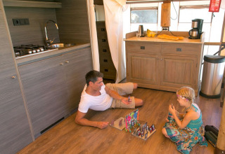 Hombre y niña juegan a un juego de mesa en el suelo de una cocina Sunlodge Safari en Camping Union Lido Mare, Italia.