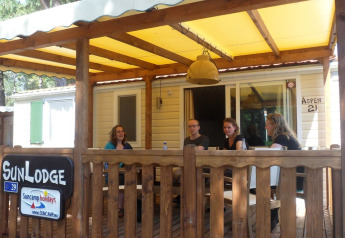 Four people sit on the porch of a SunLodge Aspen cabin at Camping Village Cavallino, Italy.