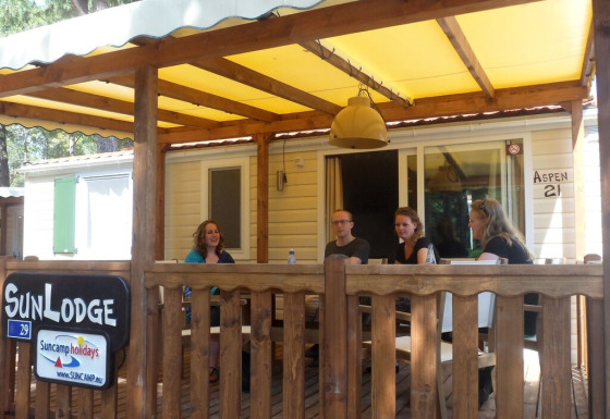 Quattro persone sedute sulla veranda di una SunLodge Aspen al Camping Village Cavallino, Italia.