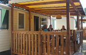 Terrasse en bois à SunLodge Aspen, Camping Village Cavallino, Italie, avec des personnes discutant.