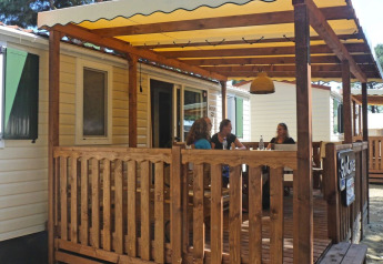 Terrasse en bois à SunLodge Aspen, Camping Village Cavallino, Italie, avec des personnes discutant.