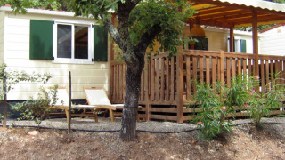 Buitenzicht op SunLodge Aspen met houten terras, groene luiken, ligstoelen en mooie begroeiing.