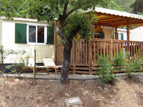 Buitenaanzicht van SunLodge Aspen met houten veranda, groene luiken, ligstoelen en groene planten.