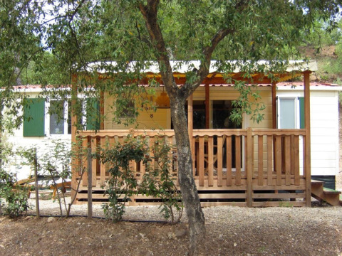 SunLodge Aspen con porche de madera en Camping Leï Suves, Francia, rodeada de vegetación y tranquilidad.