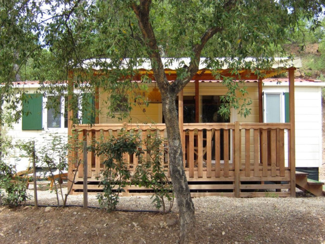 SunLodge Aspen con porche de madera en Camping Leï Suves, Francia, rodeada de vegetación y tranquilidad.