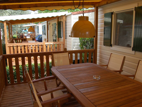 Houten terras van een lodge met tafel, stoelen en hanglamp, met zicht op andere lodges in het vakantiepark.