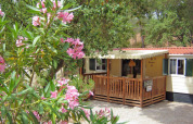 Agradable SunLodge Redwood en Camping Leï Suves, Francia, con terraza de madera y flores rosadas floreciendo.