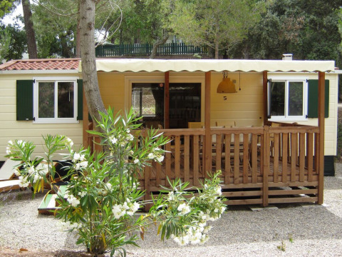 SunLodge Redwood en Camping Leï Suves, Francia, con porche de madera y arbustos en flor delante.
