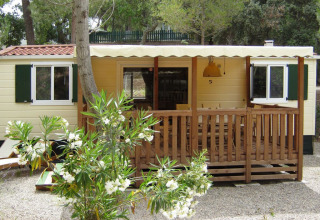SunLodge Redwood en Camping Leï Suves, Francia, con porche de madera y arbustos en flor delante.